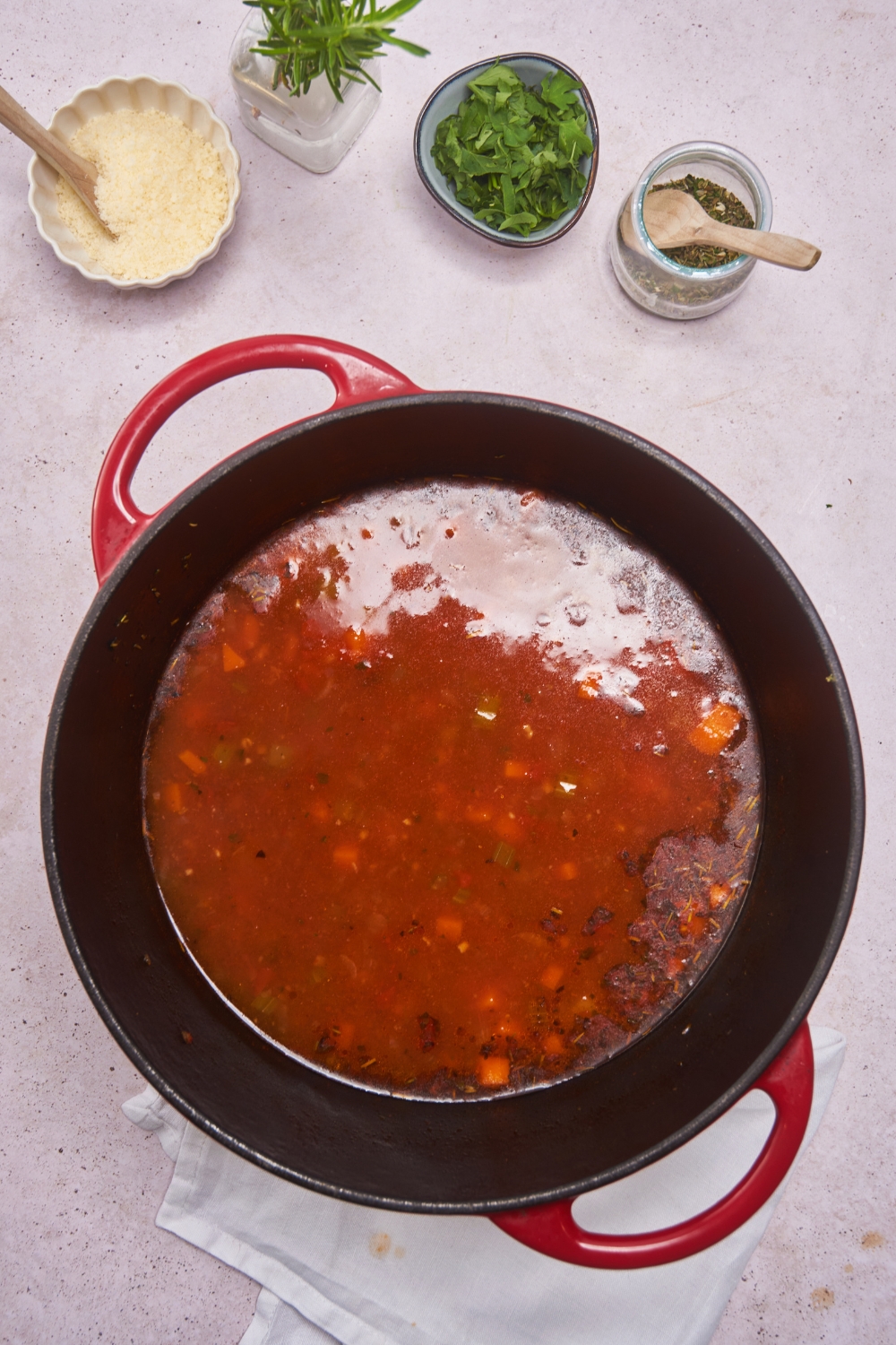 Dutch oven filled with vegetables simmering in a red broth.