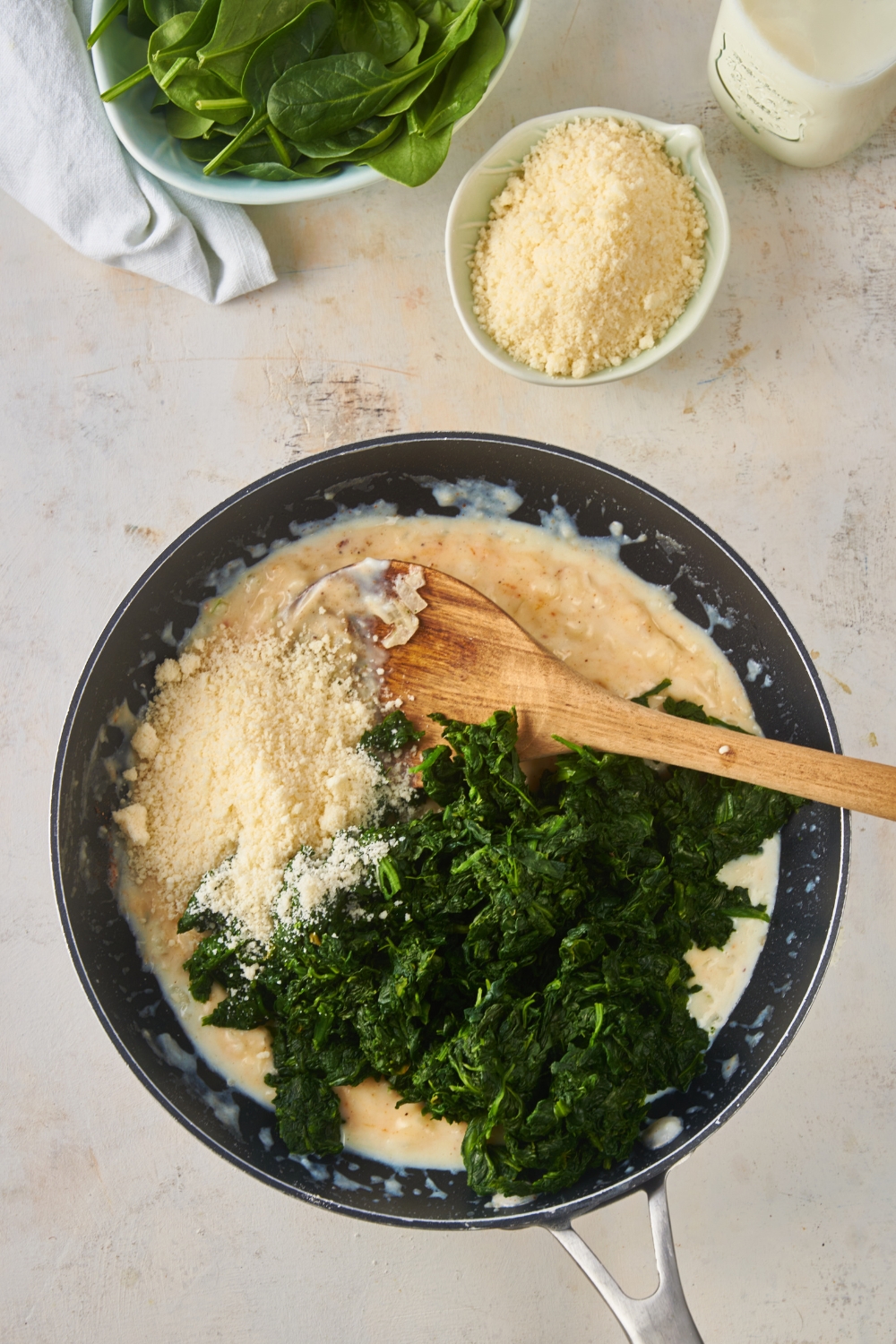 A black skillet with frozen and thawed spinach, parmesan cheese, and a creamy spiced mixture in it.