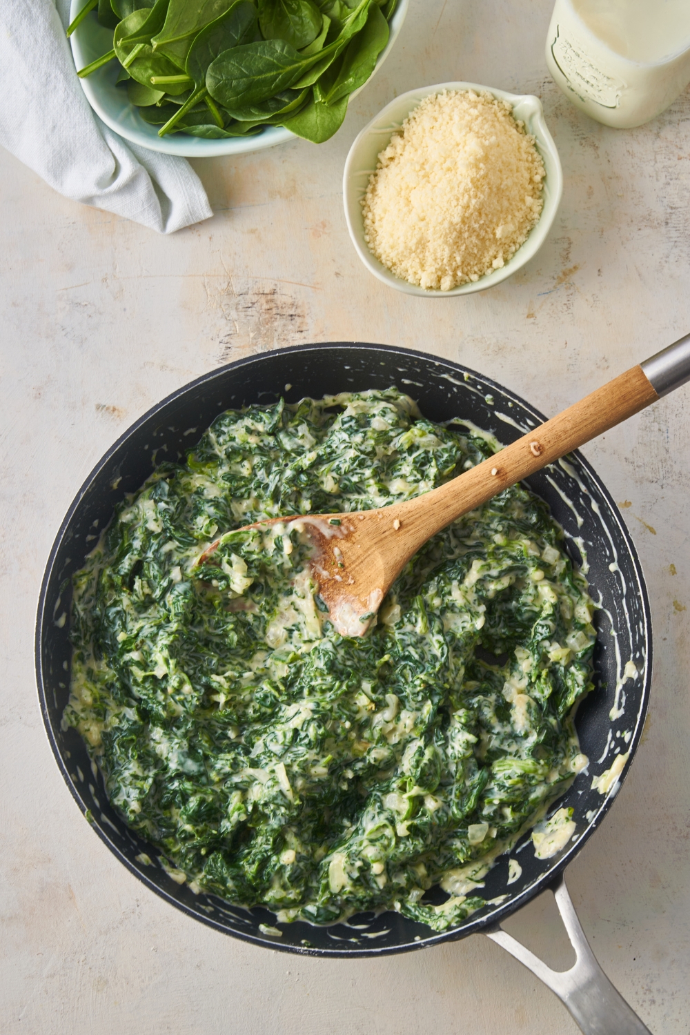 Creamed spinach in a black skillet with a wooden spoon in the skillet.