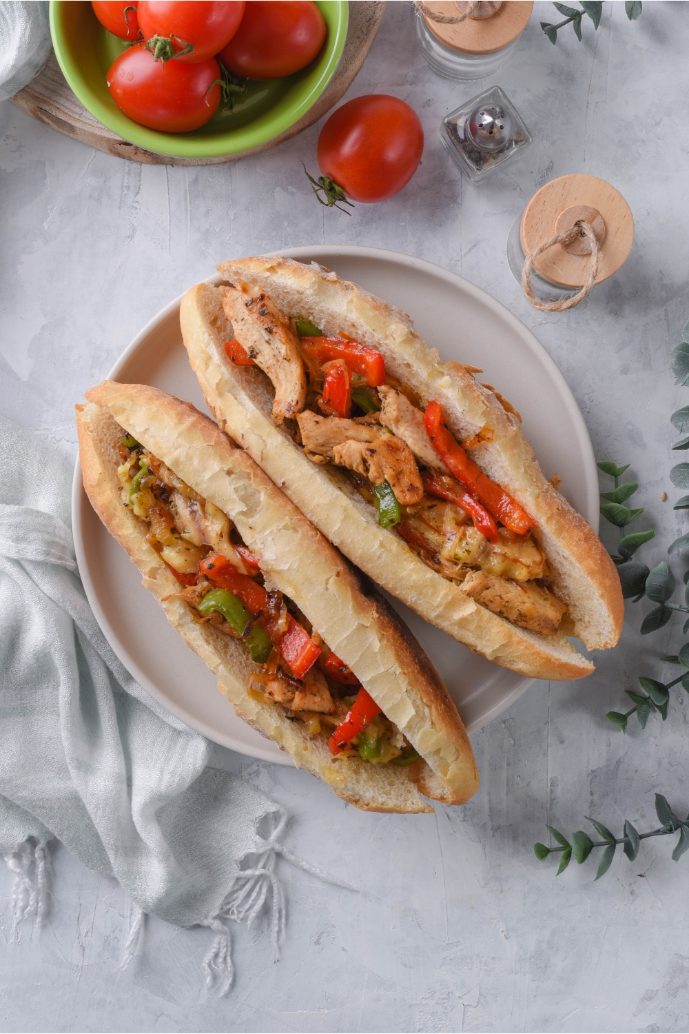 Overhead of two hoagie rolls sliced in half and stuffed with sautéed peppers, onions, and shredded chicken.