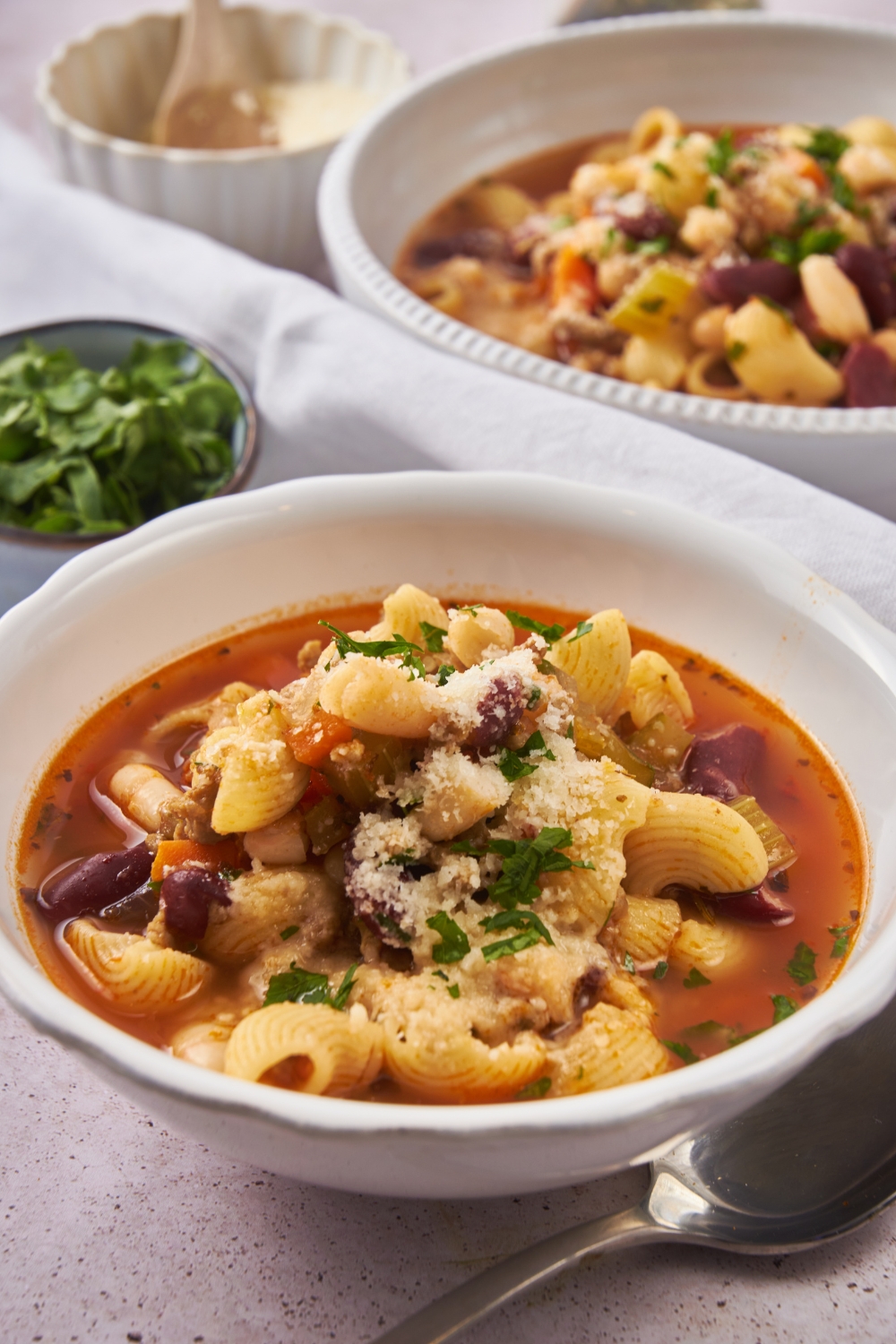 A serving of pasta e fagioli soup garnished with parmesan cheese and fresh green herbs.