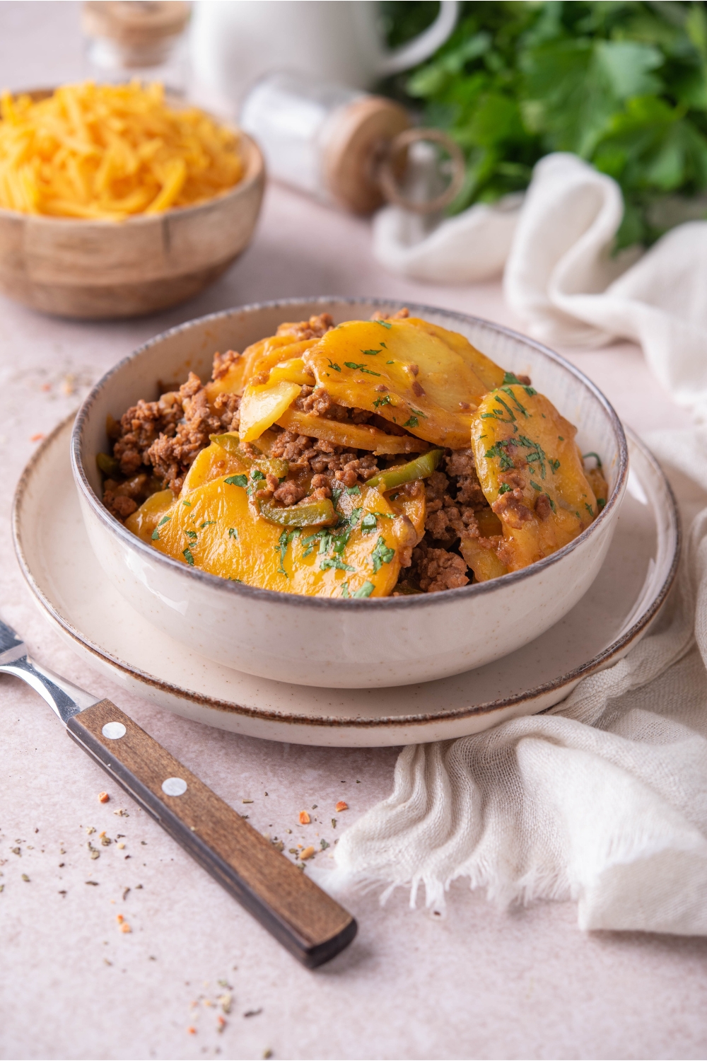 A bowl of thinly sliced potatoes with ground beef, peppers, melted cheese, and fresh herbs.