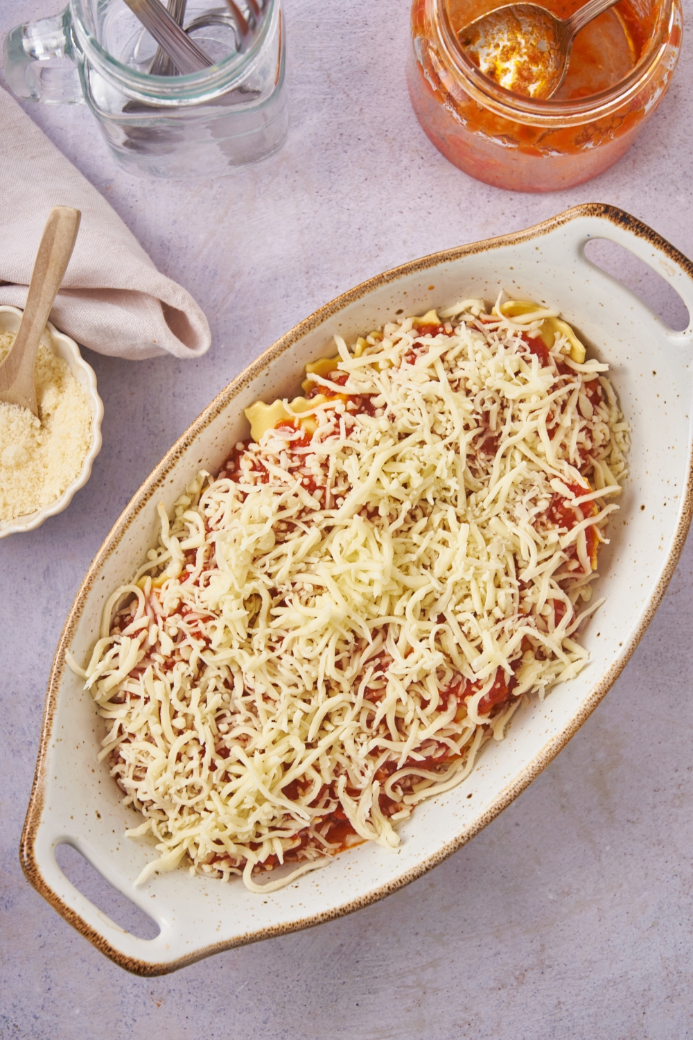 Baking dish filled with ravioli covered in red sauce and shredded cheese.