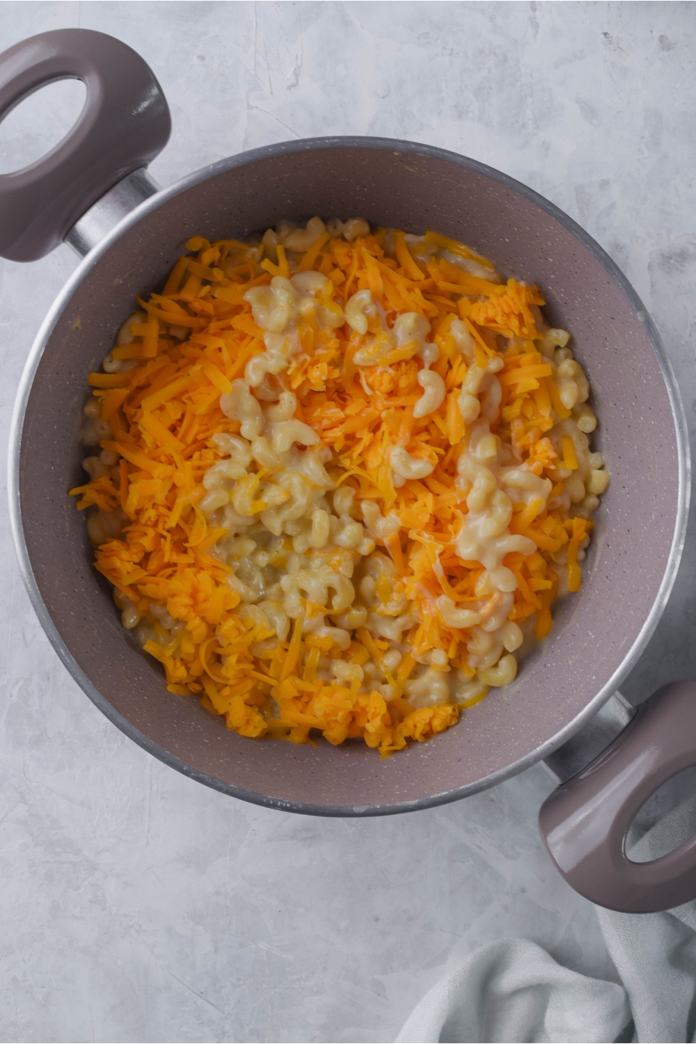 A large pot filled with cooked macaroni noodles in a creamy sauce and shredded cheese sprinkled on top.