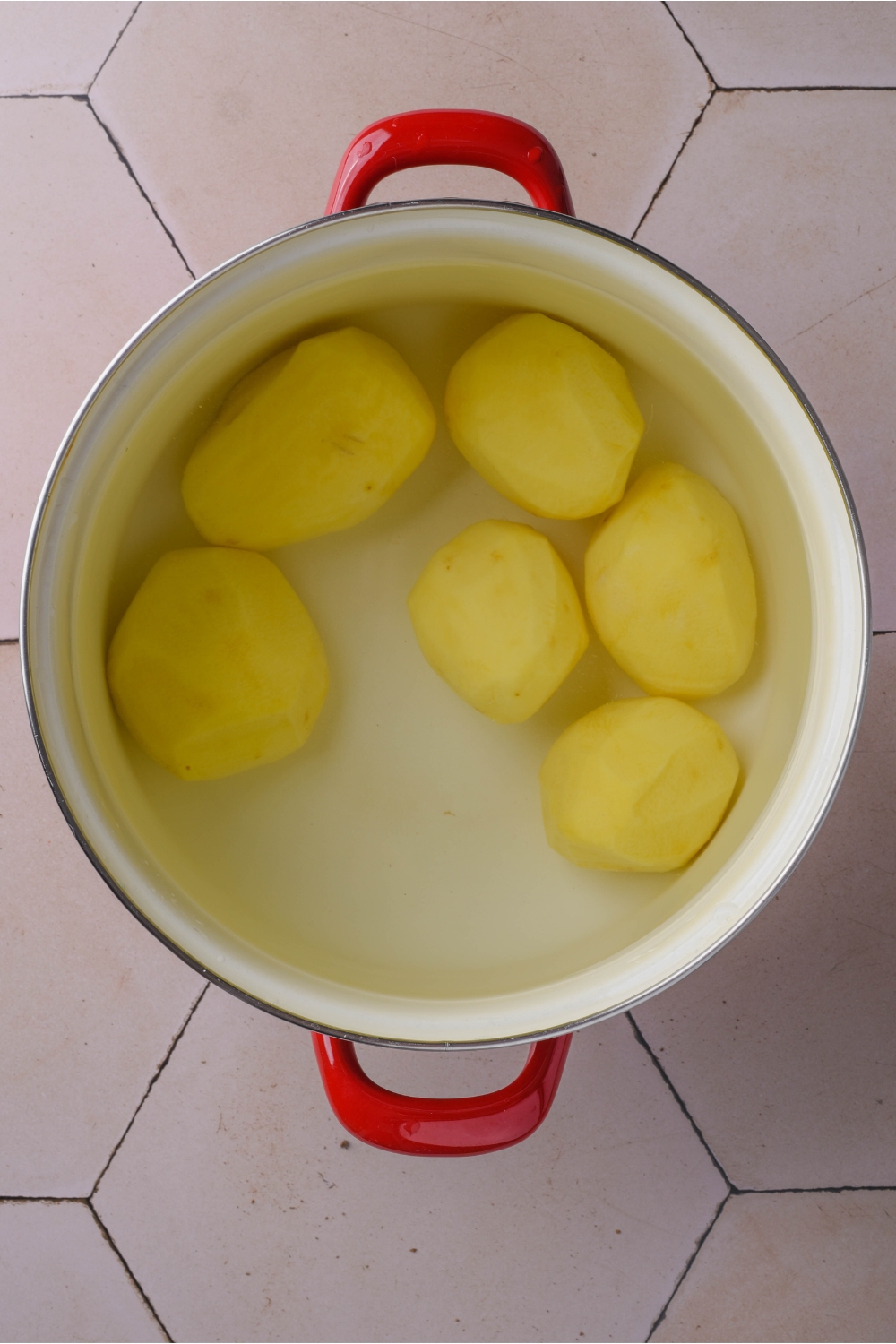 A large pot filled with six peeled potatoes and water covering the potatoes.