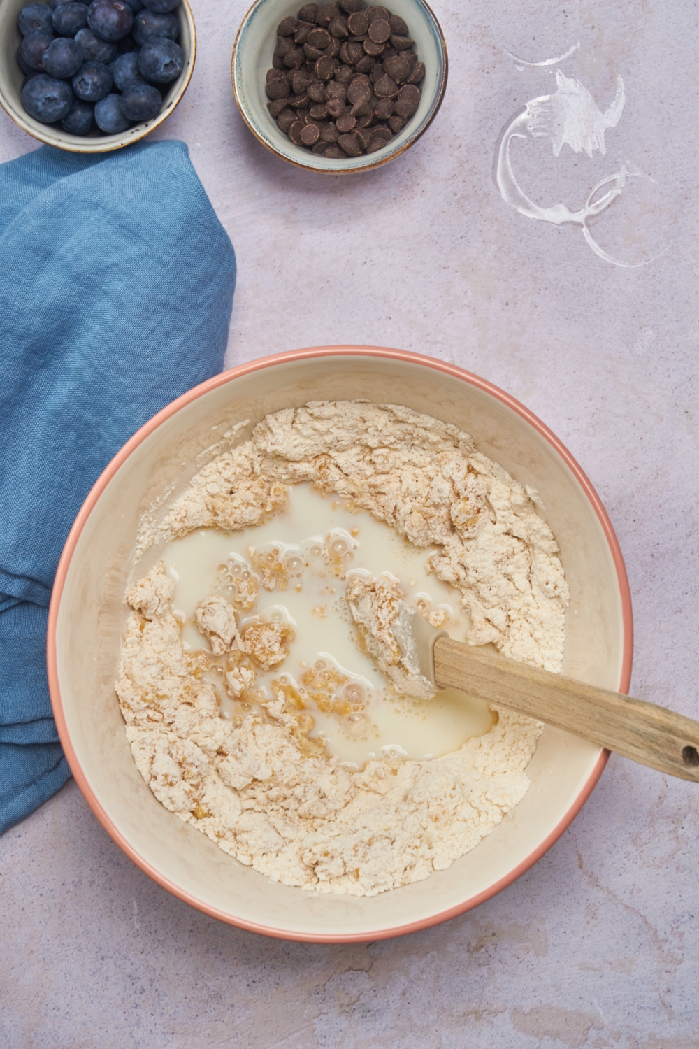 A mixing bowl with a flour mixture and milk freshly added to it. There is a silicone spatula in the bowl.