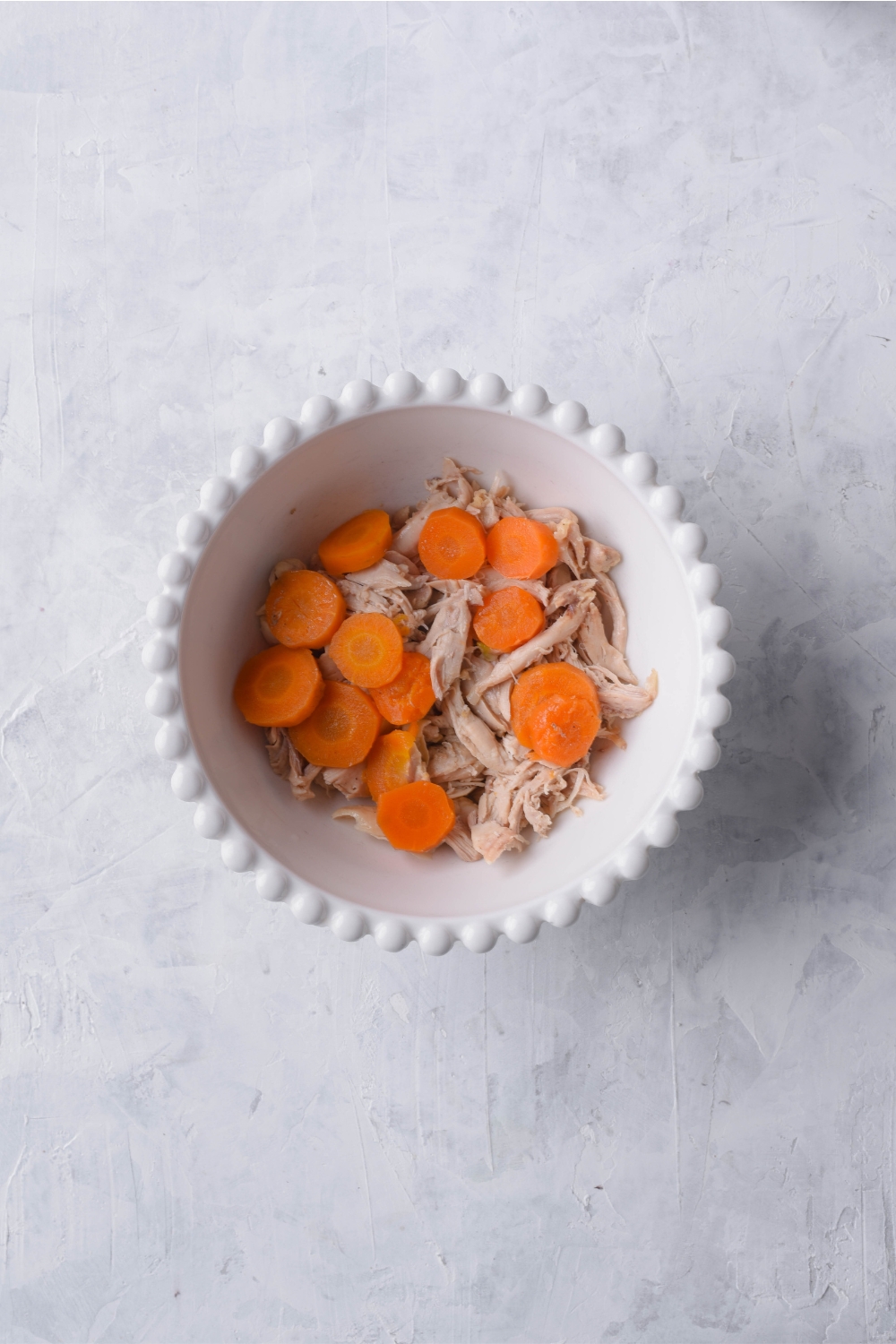 A white bowl filled with shredded chicken and cooked carrots.