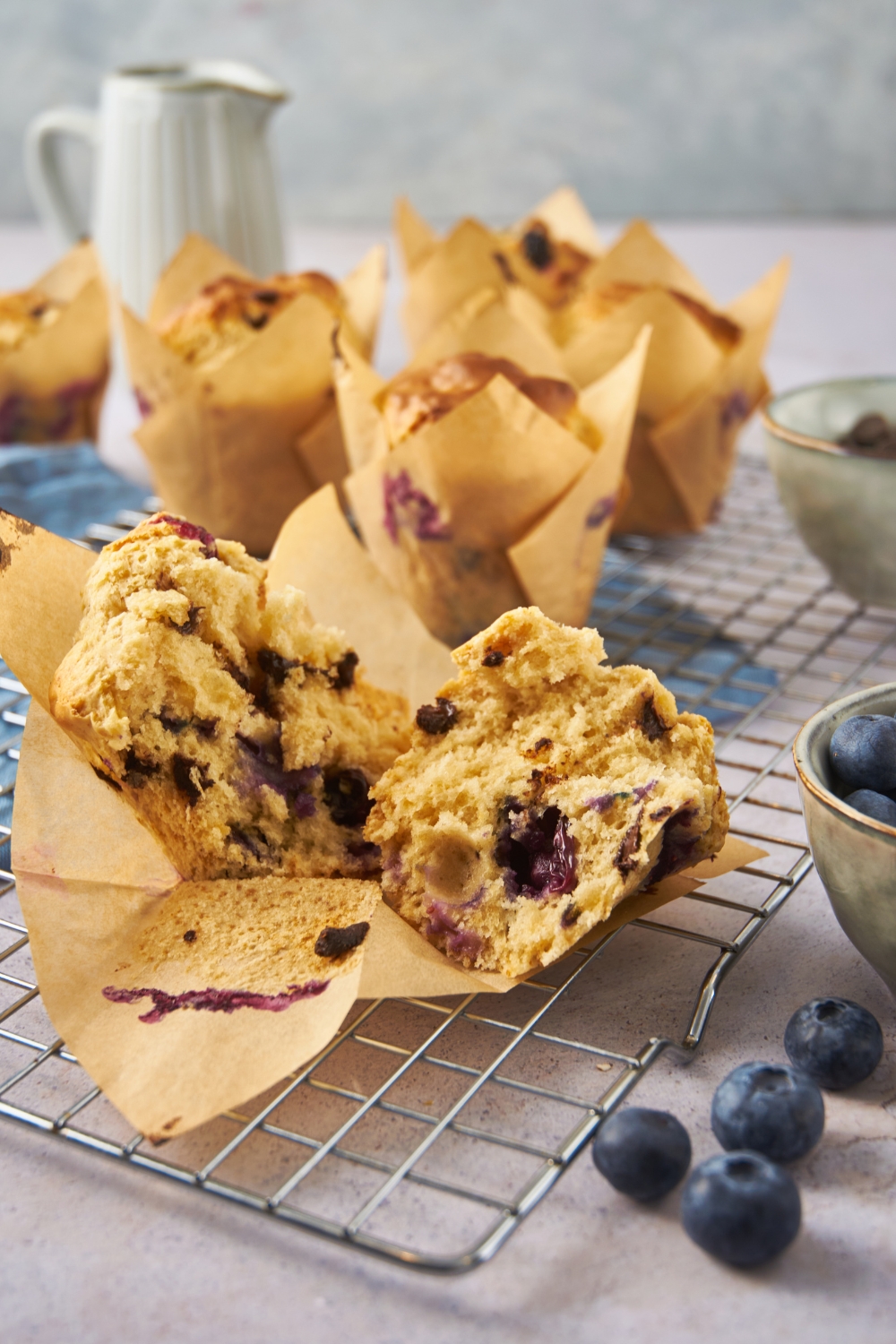 A blueberry muffin that's been cut in half and is cooling on a wire rack. The rest of the muffins are in the background.