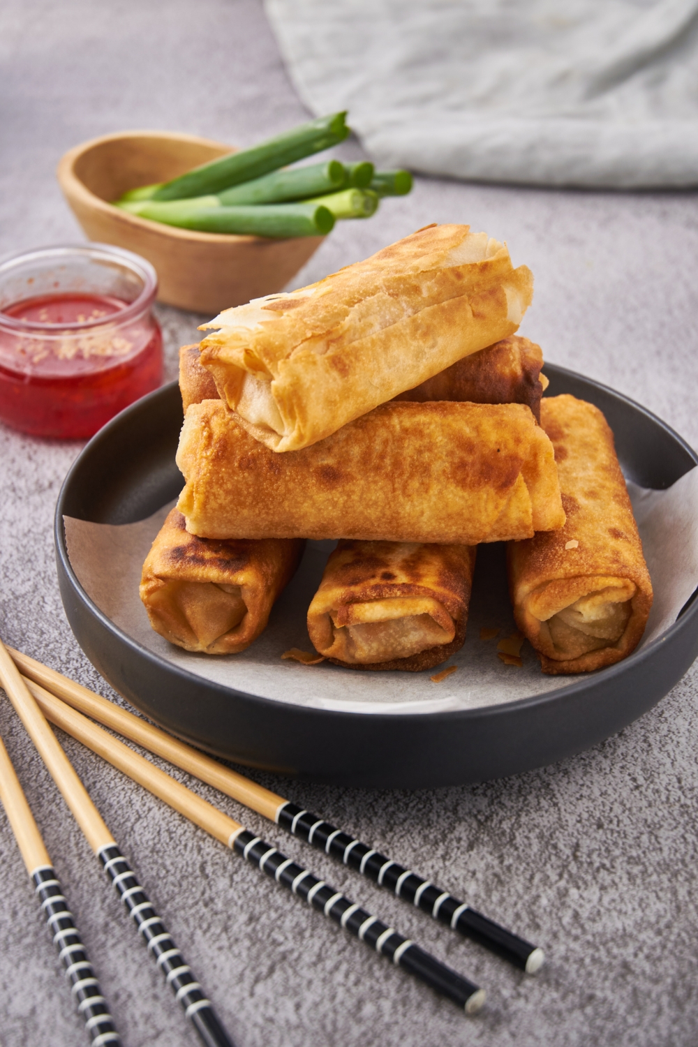 A pile of fried egg rolls stacked on top of each other on a black plate with a layer of parchment paper on the bottom.
