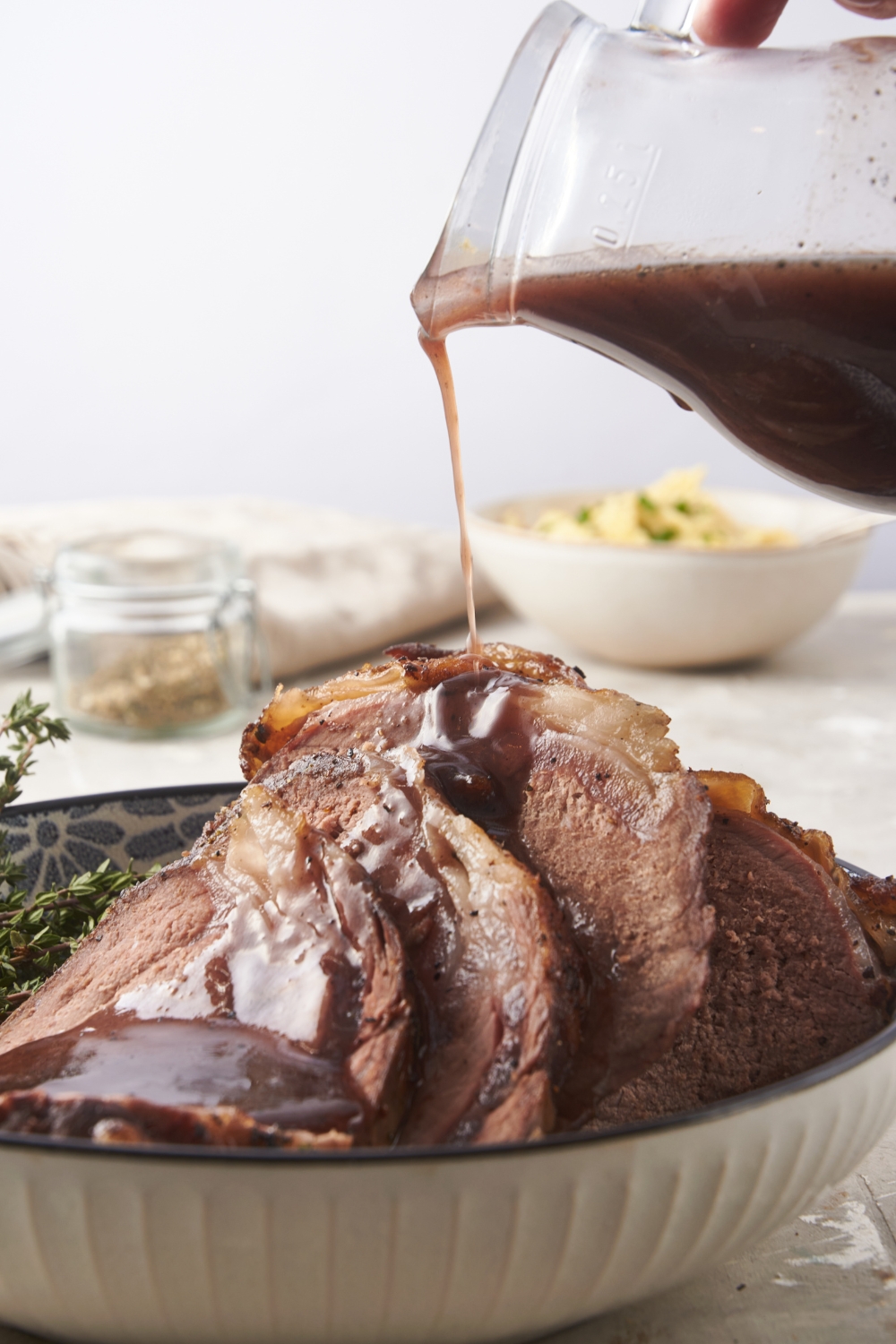 A plate of sliced prime rib layered on top of each other with a bottle of gravy being poured over top of the beef.