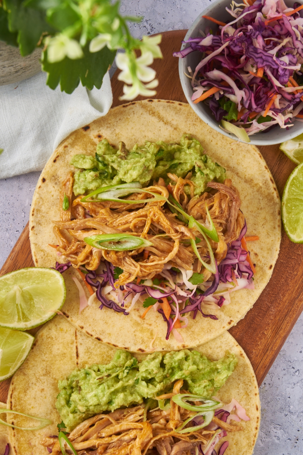 Close up of a pulled pork taco with scallions, slaw, and guacamole on it.