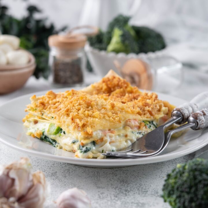 A serving of vegetable lasagna with cream sauce and a crispy cracker crumb topping on a plate with two forks.
