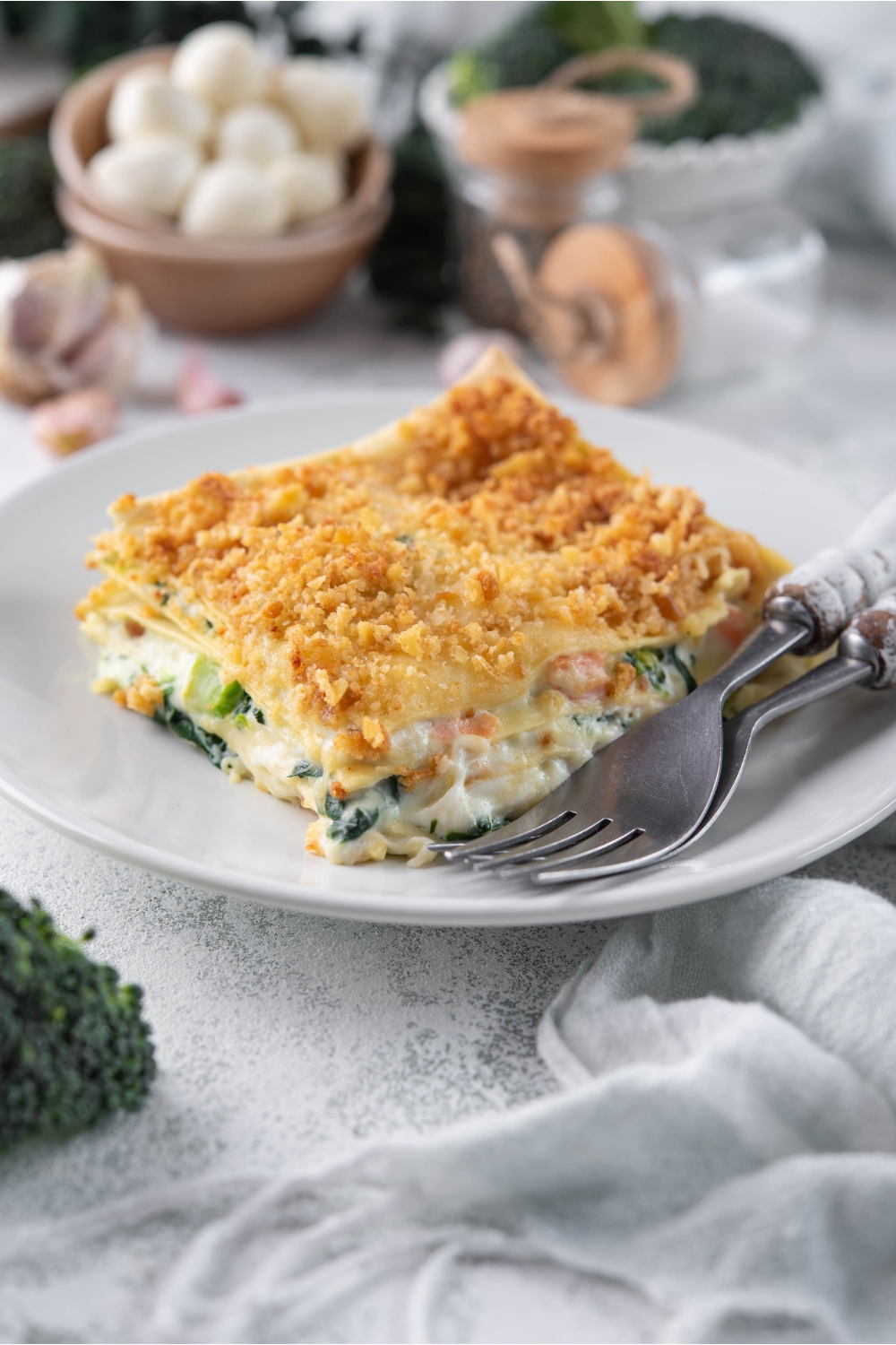 A serving of vegetable lasagna with cream sauce and a crispy cracker crumb topping on a plate with two forks.