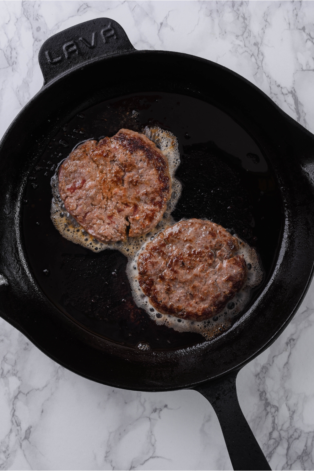 A cast iron skillet with two hamburger patties being cooked in it.