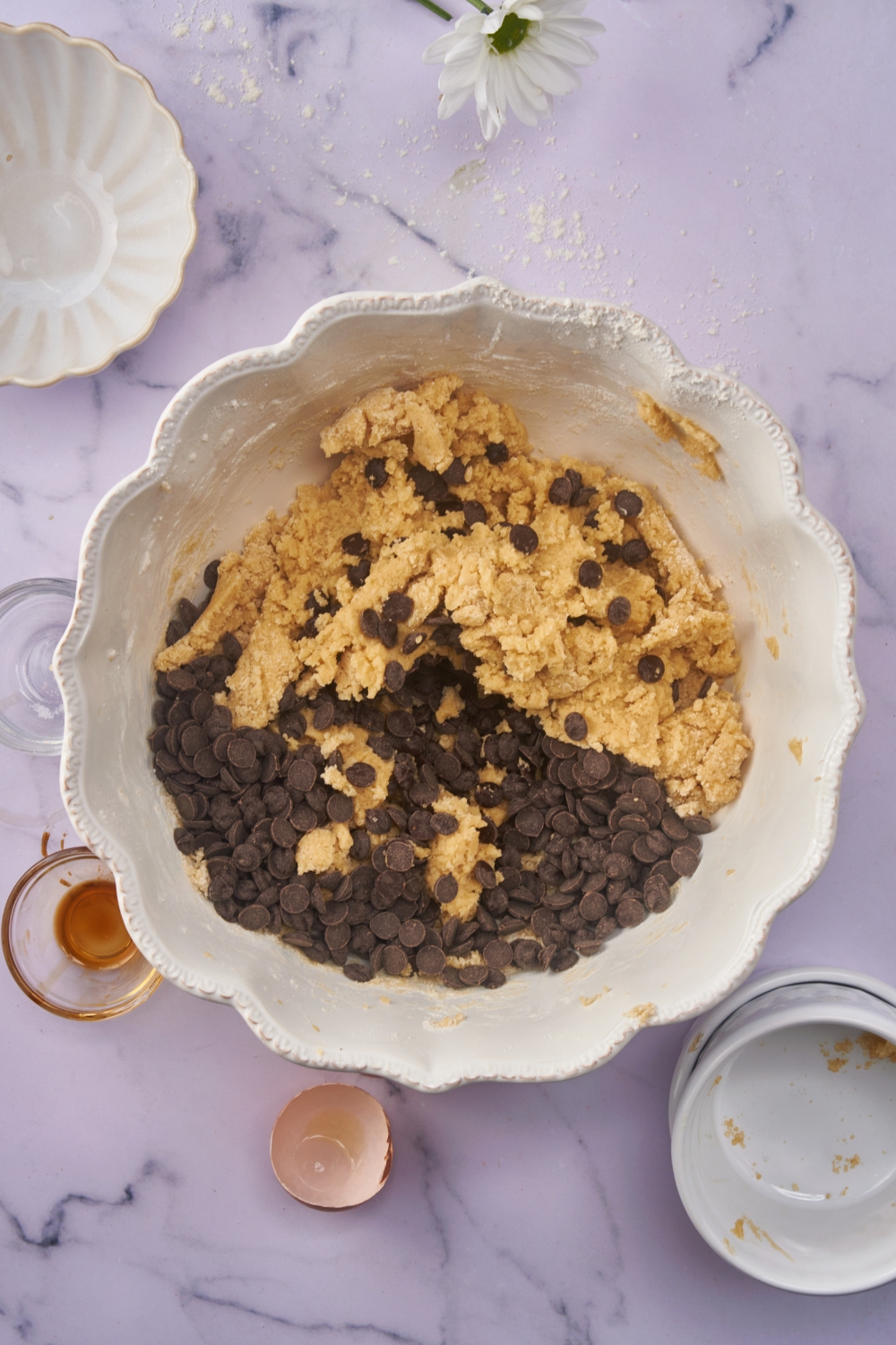 A white mixing bowl with cookie batter and chocolate chips in it but not fully combined.