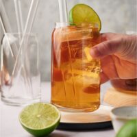 A hand grabbing a glass of iced tea off a plate. The glass has a straw and a lime wedge in it.