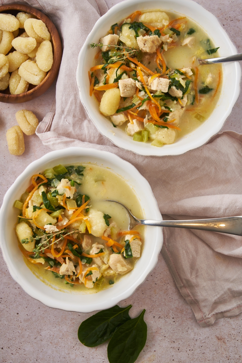 Overhead view of two bowls of chicken gnocchi soup with spinach, diced celery, and shredded carrots in them.