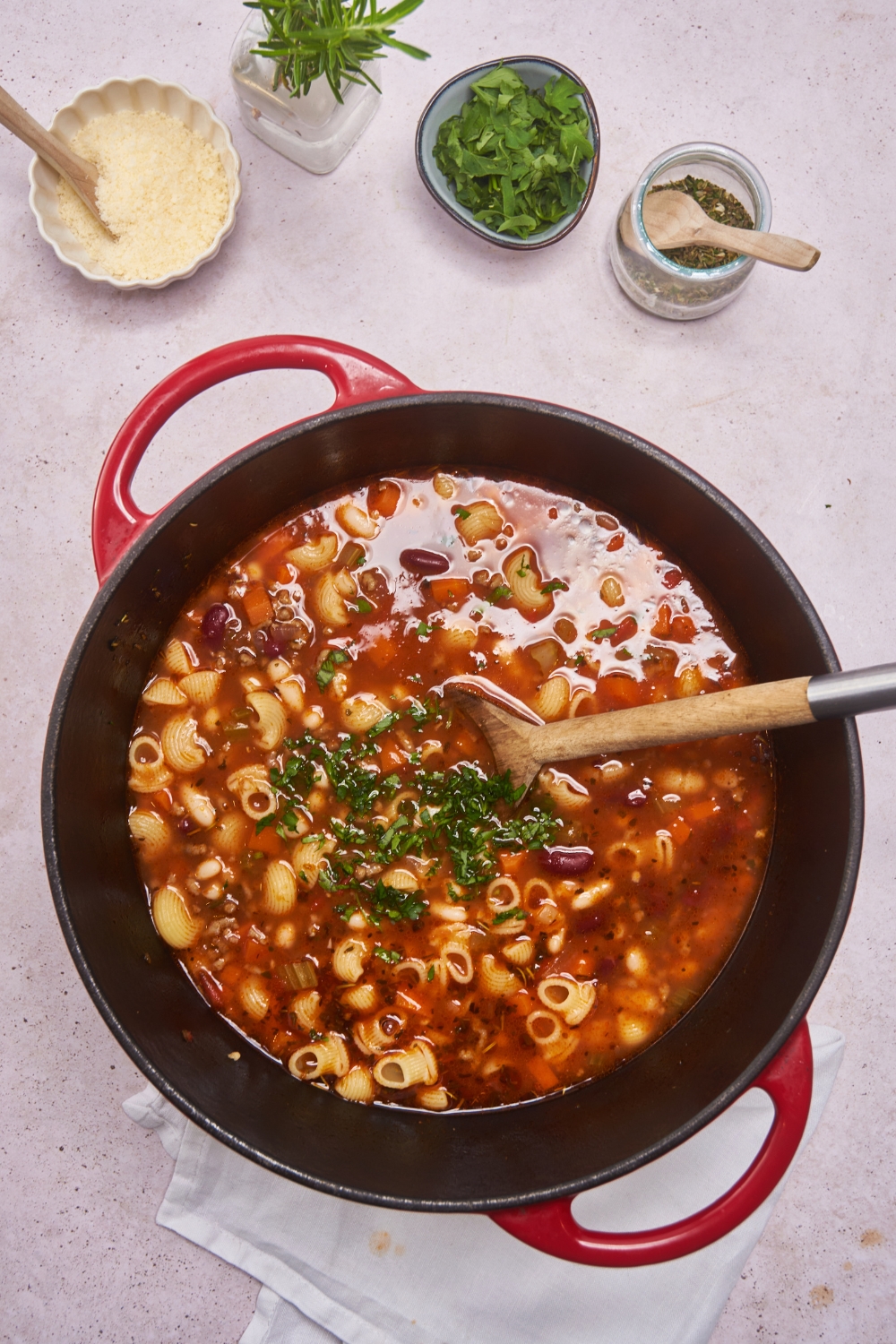 Dutch oven filled with pasta noodles, vegetables, beans, and fresh green herbs simmering in a tomato broth.