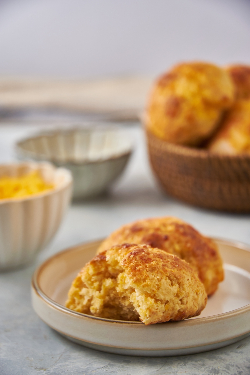 A plate with two cheddar biscuits, one with a bite taken out. In the background is a basket with more biscuits.