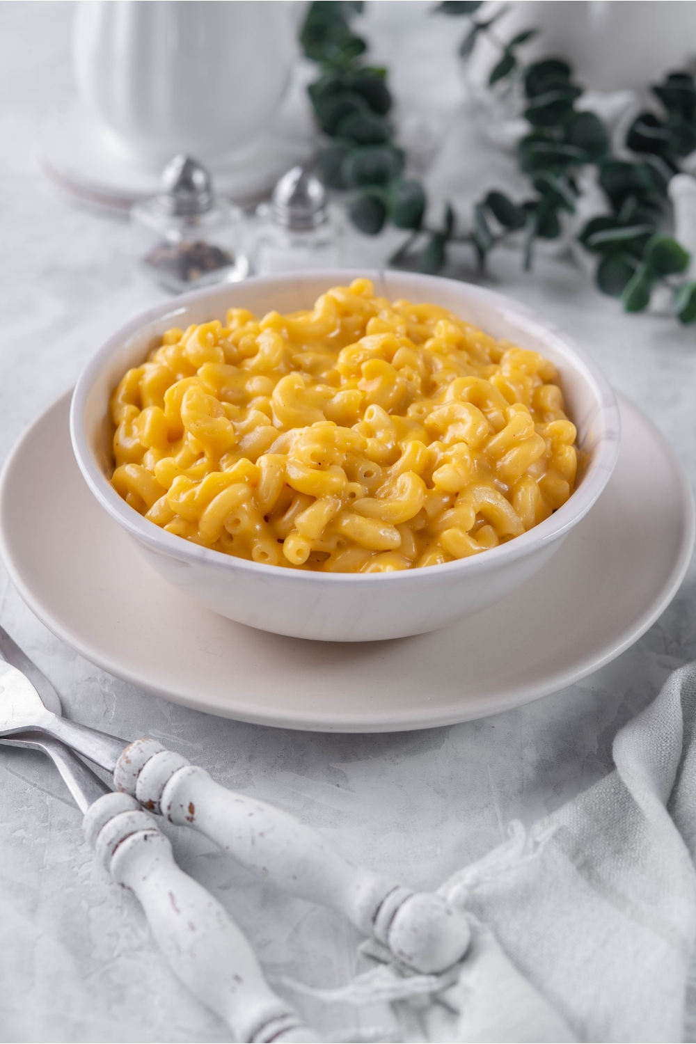 A bowl of creamy macaroni and cheese on a plate with two forks next to it.