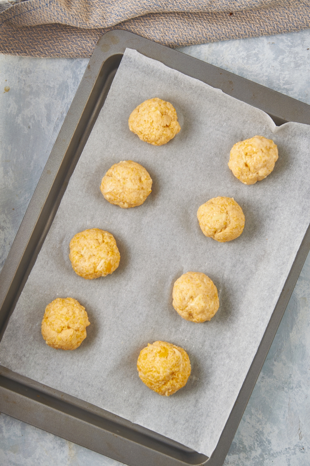 Eight equal-sized balls of dough on a baking sheet lined with parchment paper.