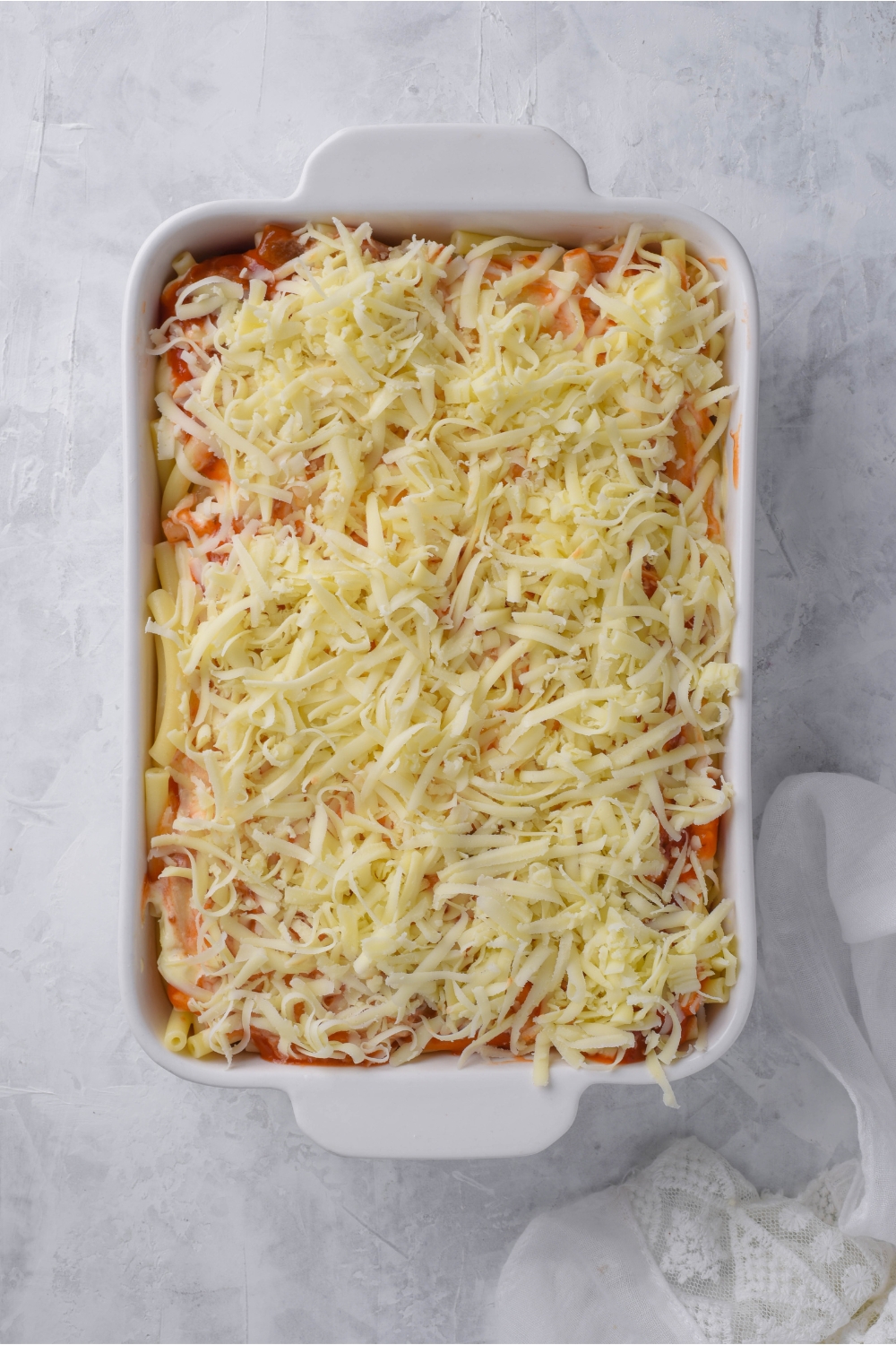 A white casserole dish filled with unbaked ziti topped with shredded mozzarella cheese.