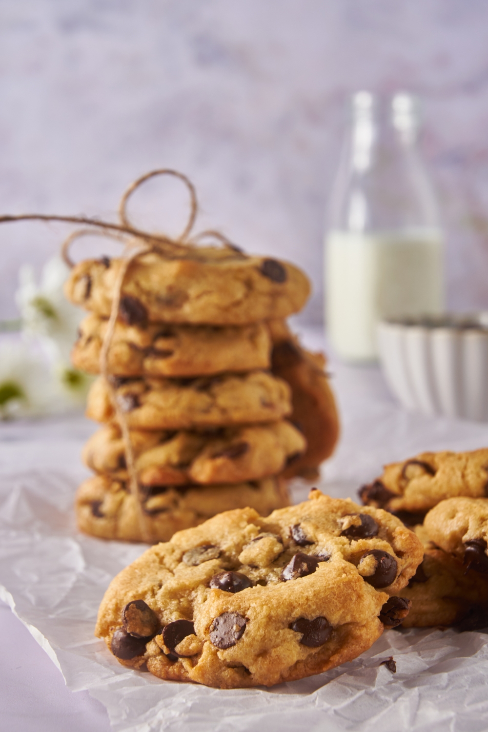 A pile of chocolate chip cookies with a stack of cookies tied with twine in the background.