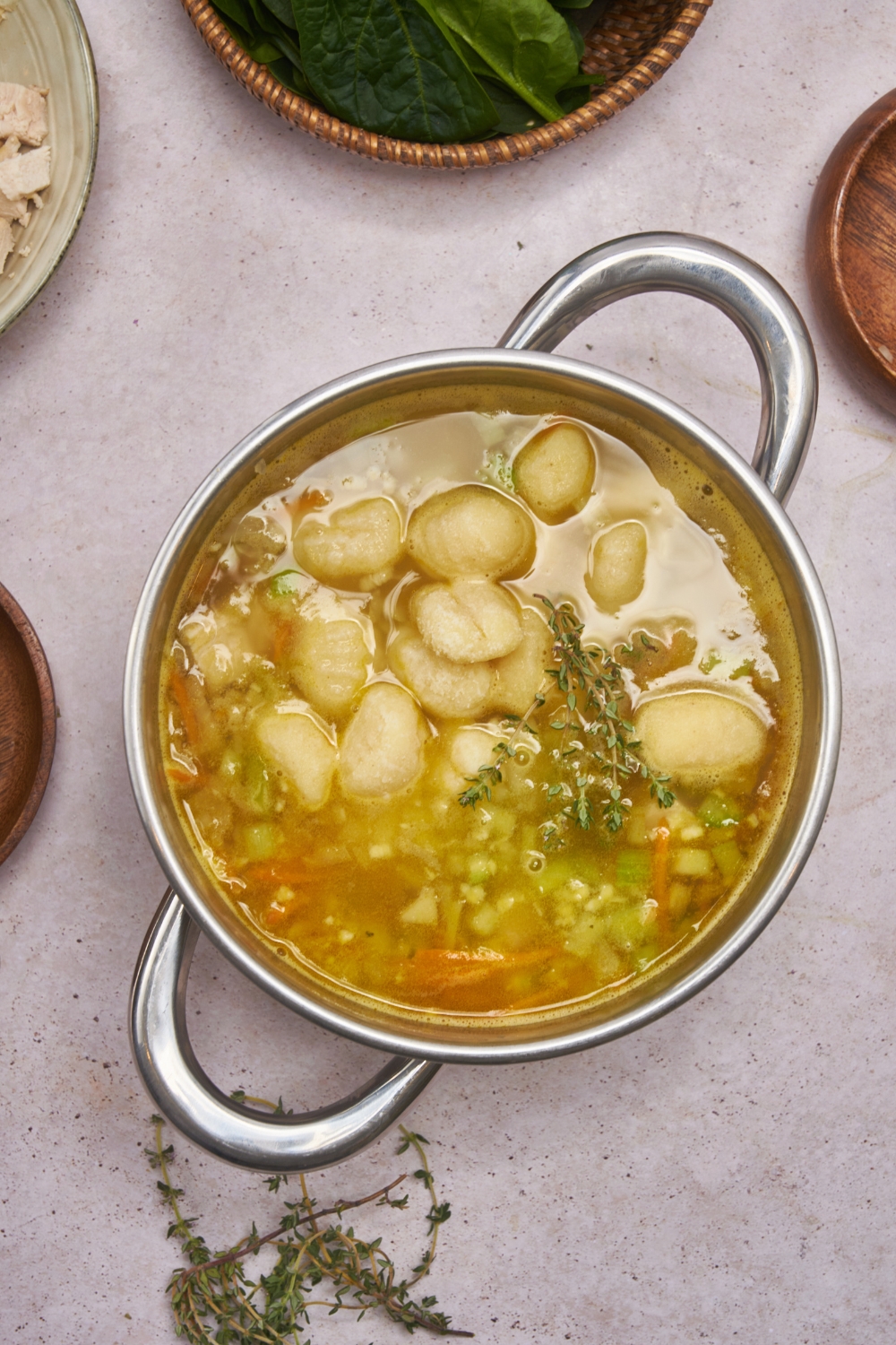 Large pot with potato gnocchi, diced celery, carrots, and fresh herbs simmering in chicken broth.