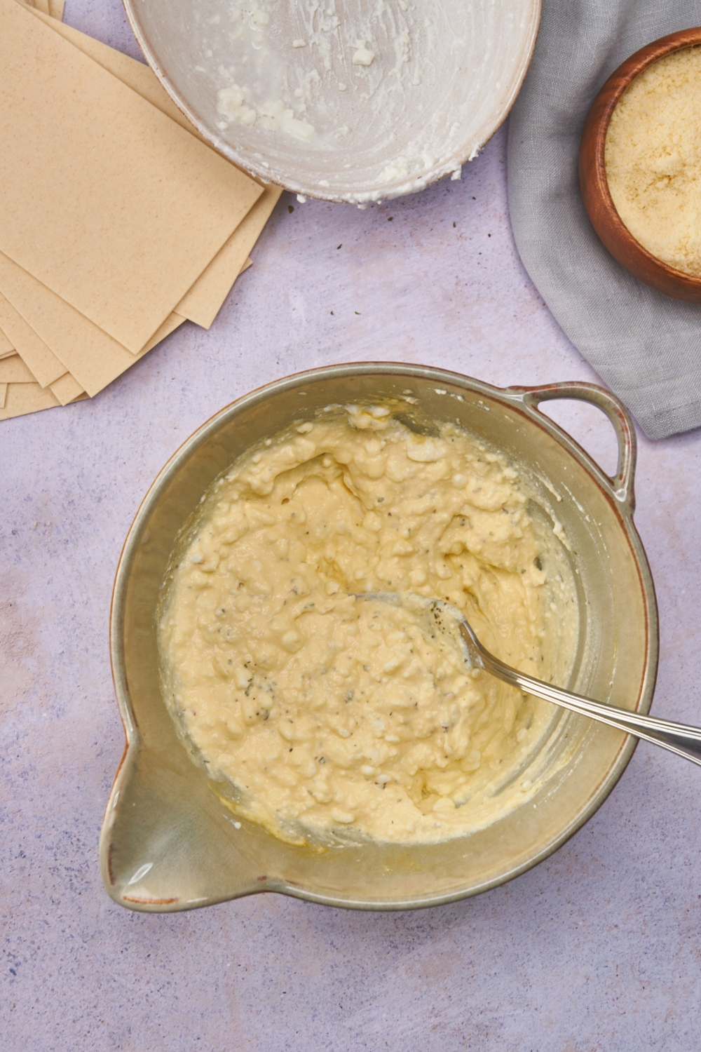 Mixing bowl filled with ricotta and seasonings added and combined with a spoon.