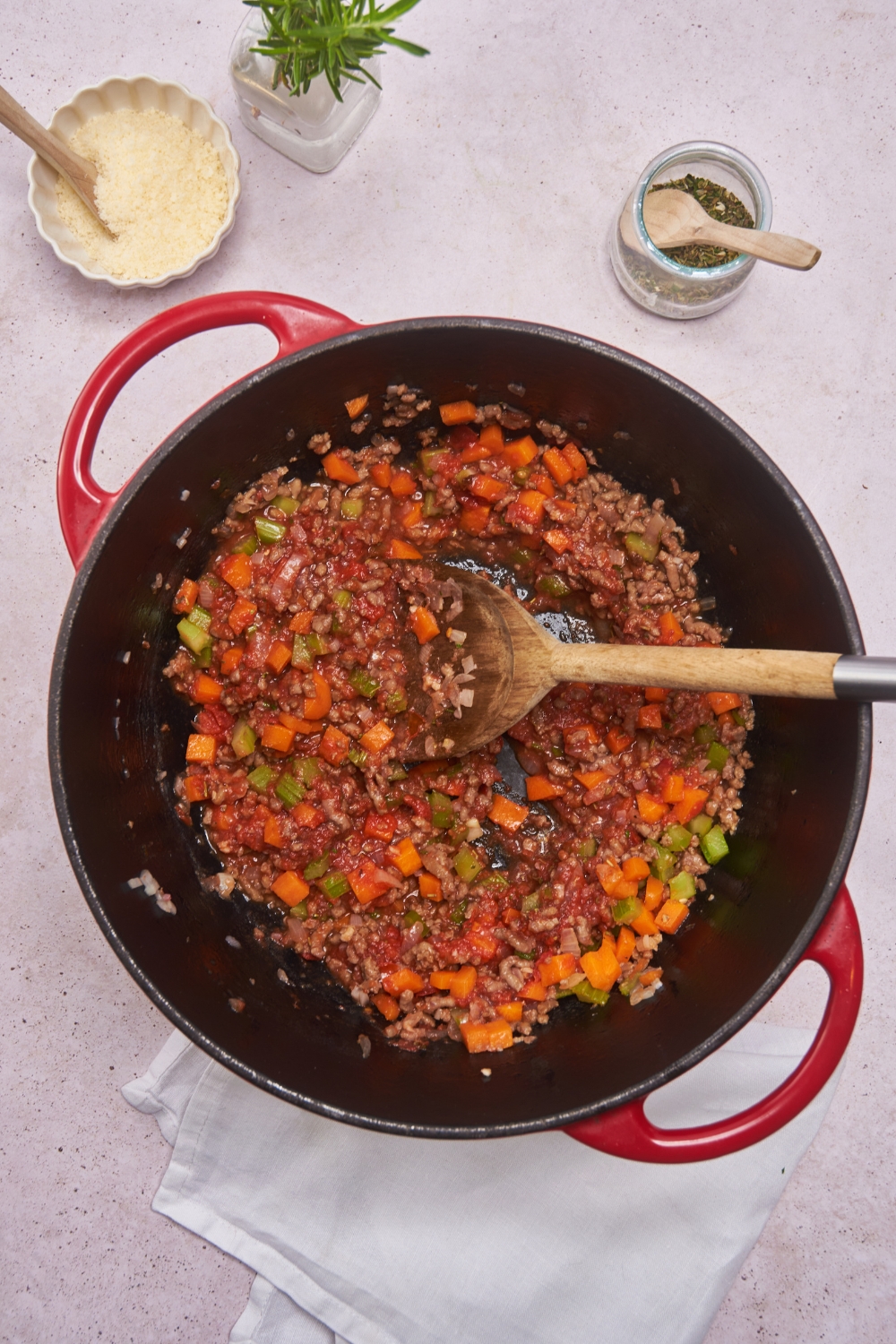 Dutch oven filled with cooked ground beef, diced carrots, tomatoes, celery, red sauce, and Italian seasoning.