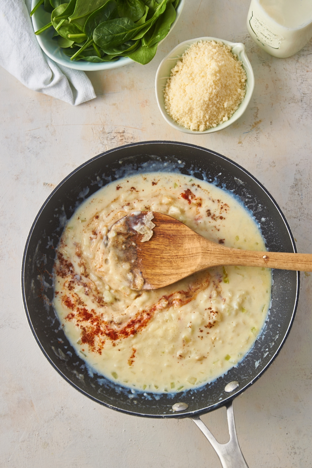 A black skillet with a diced onion and cream sauce in it along with a wooden spoon and a dash of paprika.