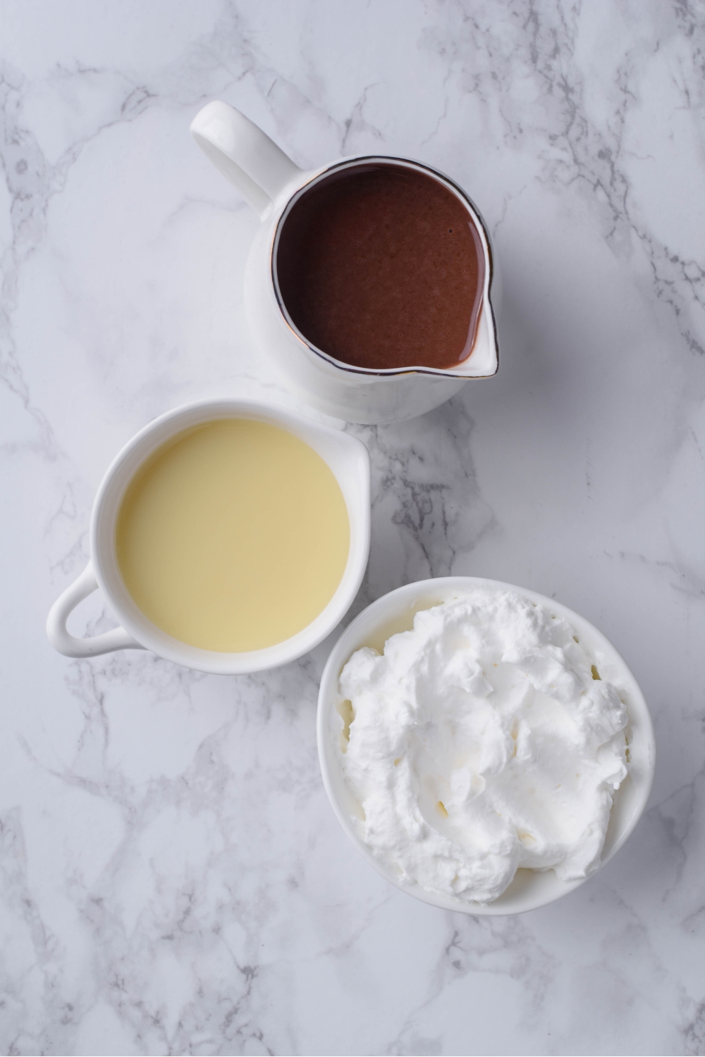 Overhead view of a pitcher of chocolate milk, a bowl of cool whip, and a bowl of condensed milk.