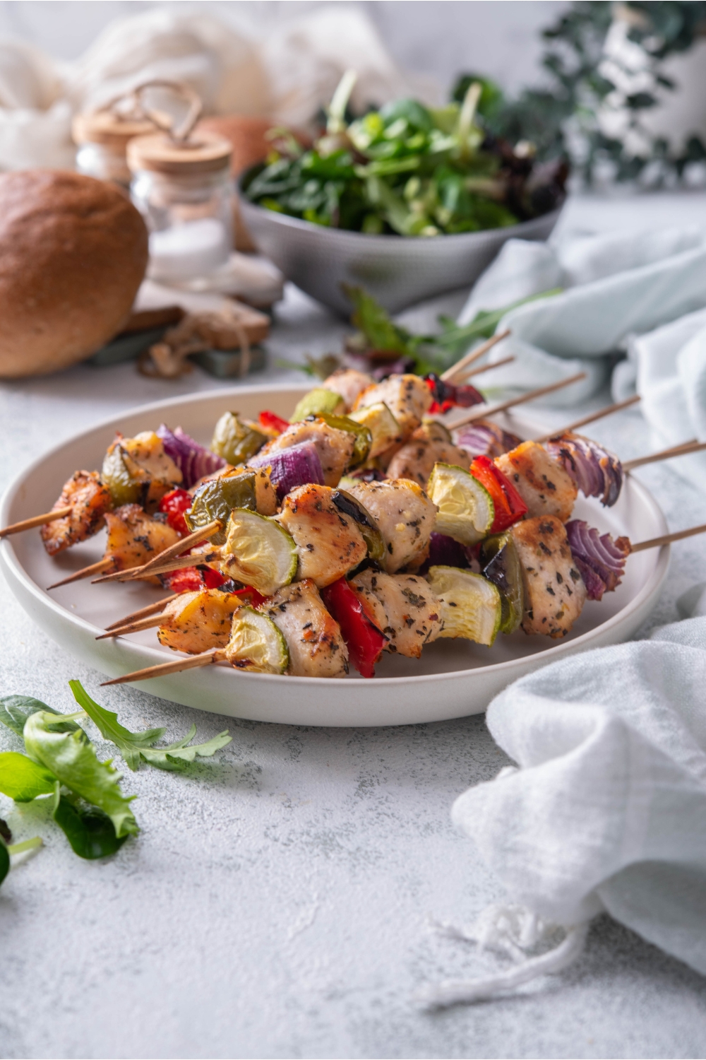 A plate of six chicken and vegetable skewers with red onion, bell pepper, and zucchini in the skewers.