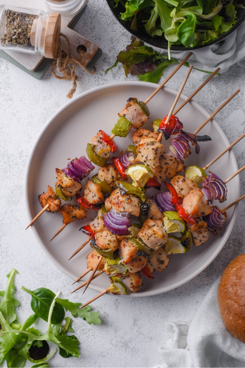Overhead view of a plate of six chicken and vegetable skewers with red onion, bell pepper, and zucchini in the skewers.