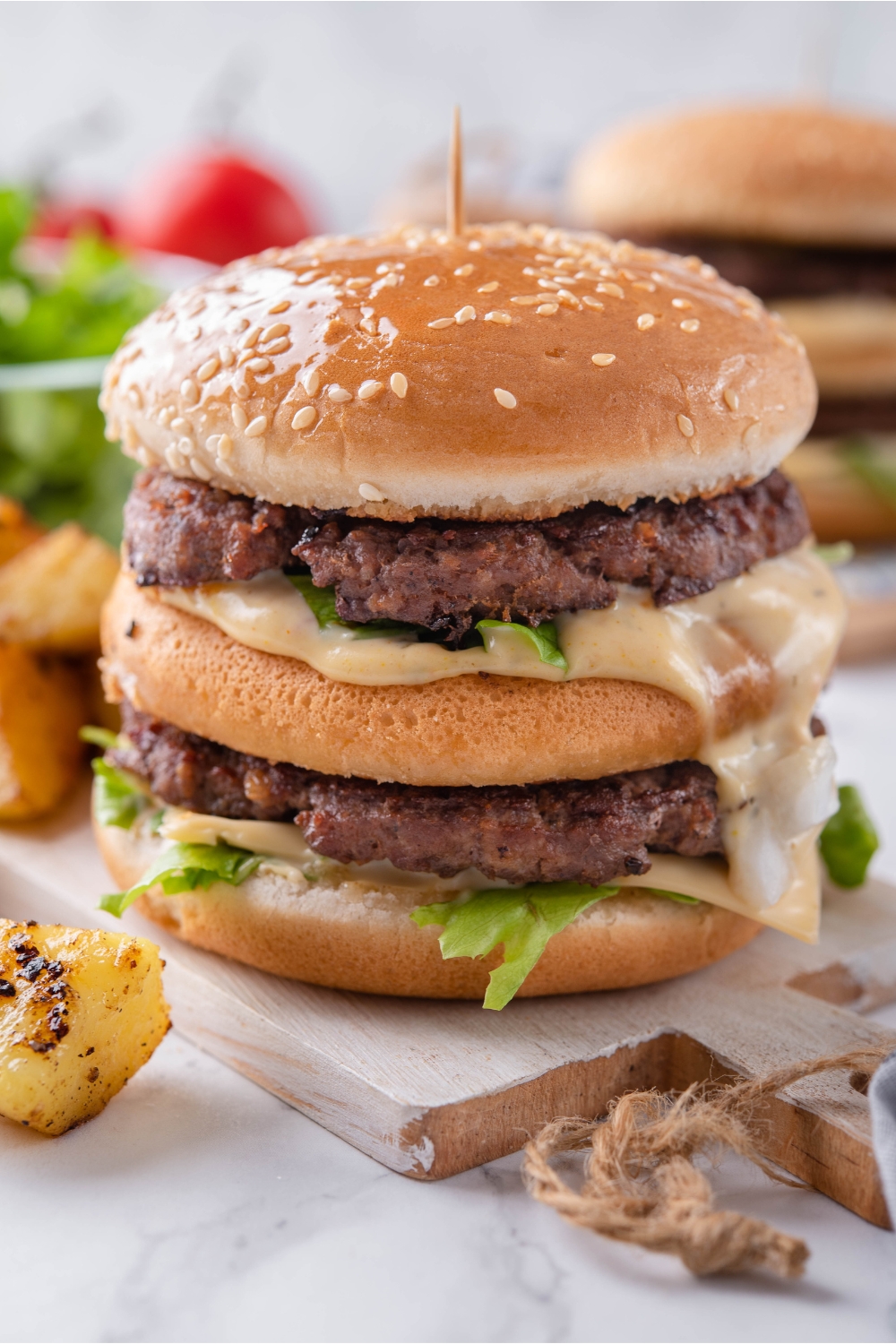 Close up of a McDonald's big mac on a wooden board with big mac sauce dripping off the side and a toothpick stuck in the center of the burger.