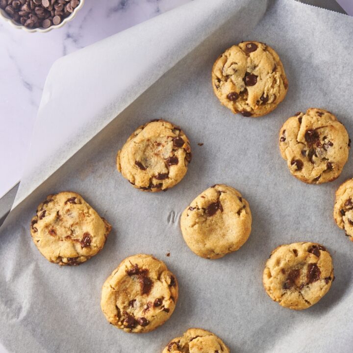 Freshly baked chocolate chip cookies on a baking sheet lined with parchment paper.