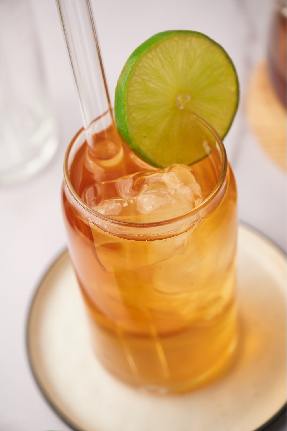Close up of a glass of iced tea with ice cubes and a straw in it, garnished with a lime wheel.