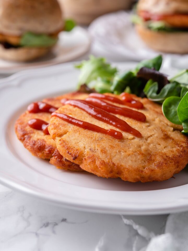 Close up of two fried salmon patties layered on top of each other and both covered with a drizzle of ketchup.