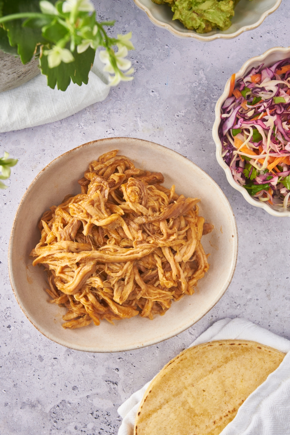 A bowl of BBQ pulled pork next to a pile of tortillas and a bowl of slaw.