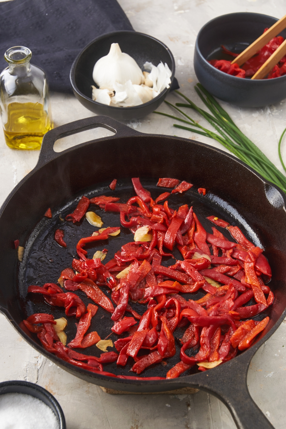A cast iron skillet with sautéed red bell peppers and garlic in it.