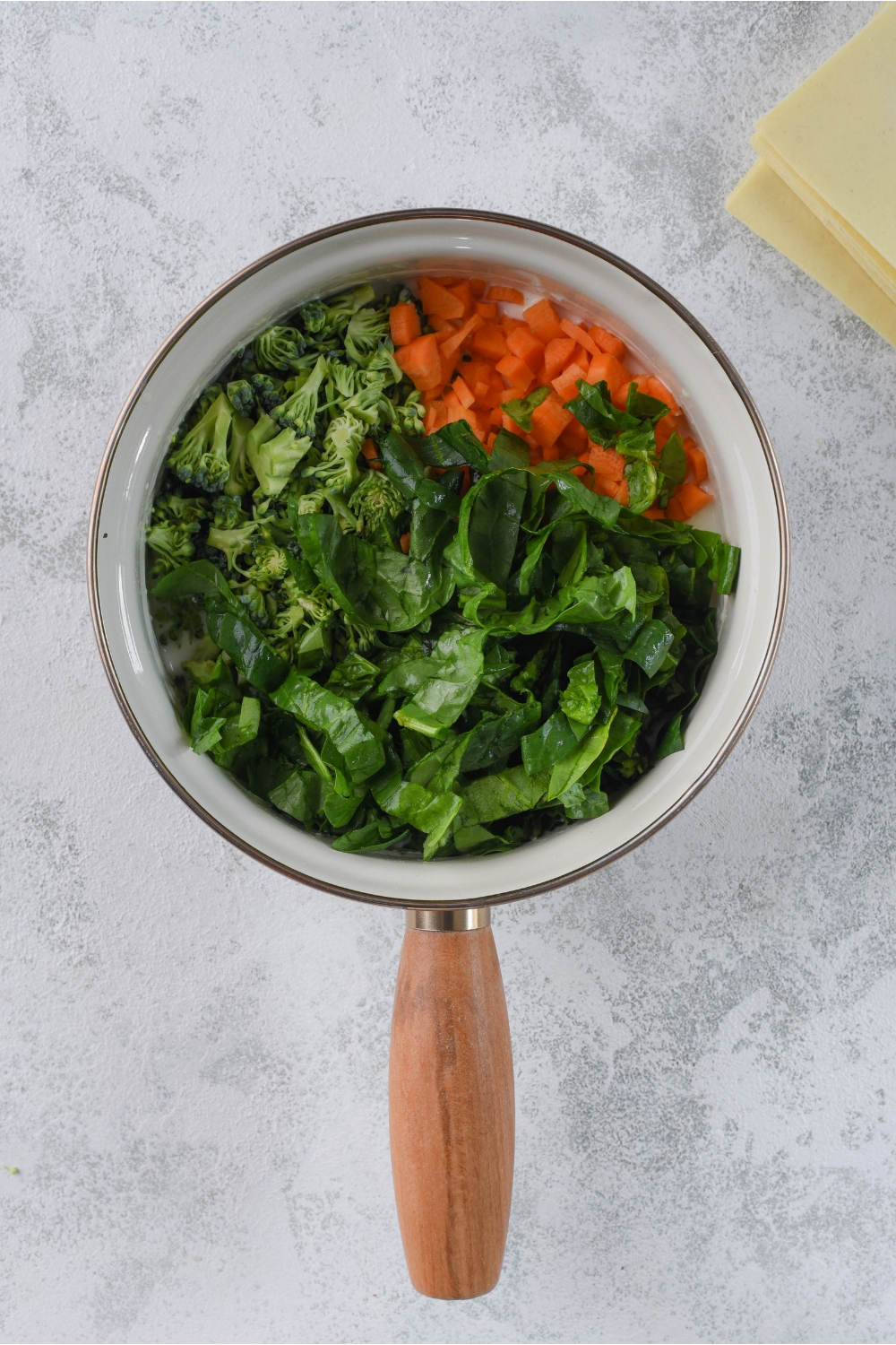 A pot with fresh spinach, diced carrots, and diced broccoli in it.