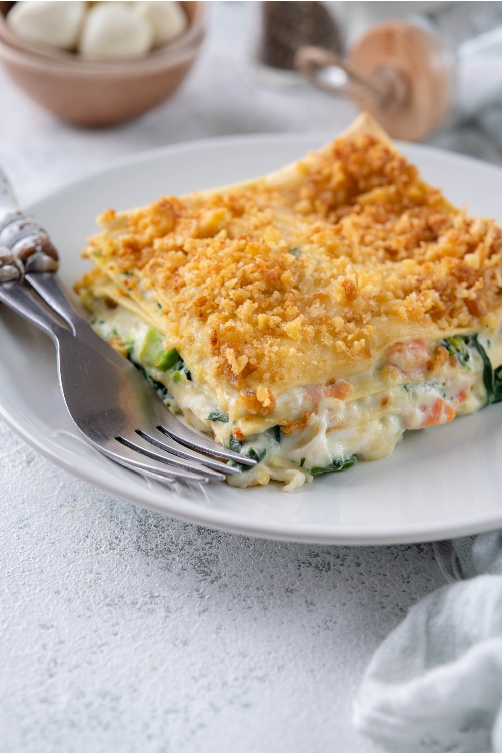 A serving of vegetable lasagna with cream sauce and a crispy cracker crumb topping on a plate with two forks.