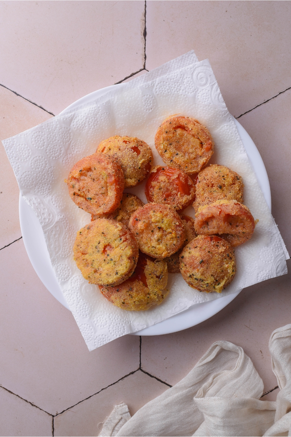 A pile of fried red tomatoes on a plate lined with paper towels.