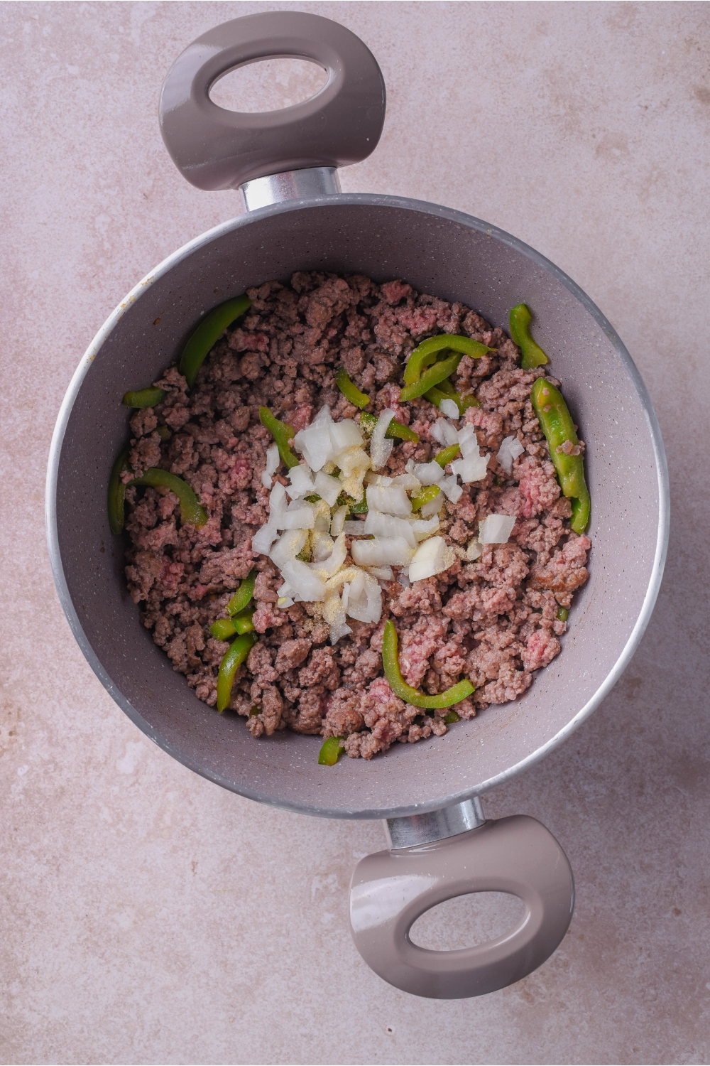 Large grey pot filled with cooked ground beef, sliced green peppers, and diced onions in the center of the pot.