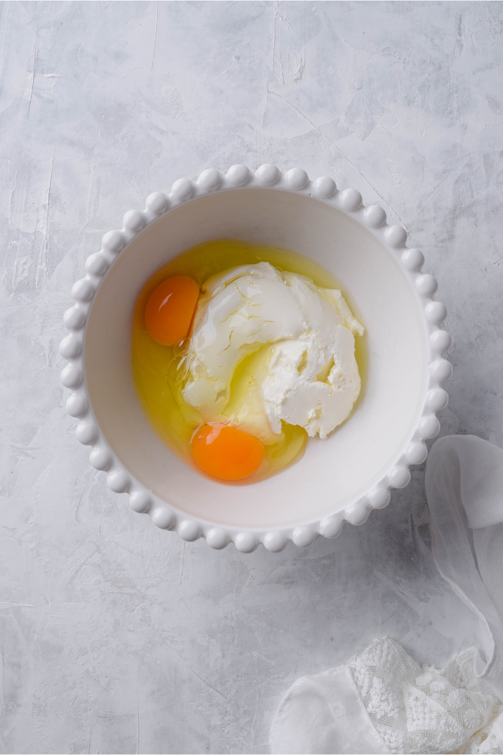 A white bowl with cream cheese and two unbeaten eggs in it.