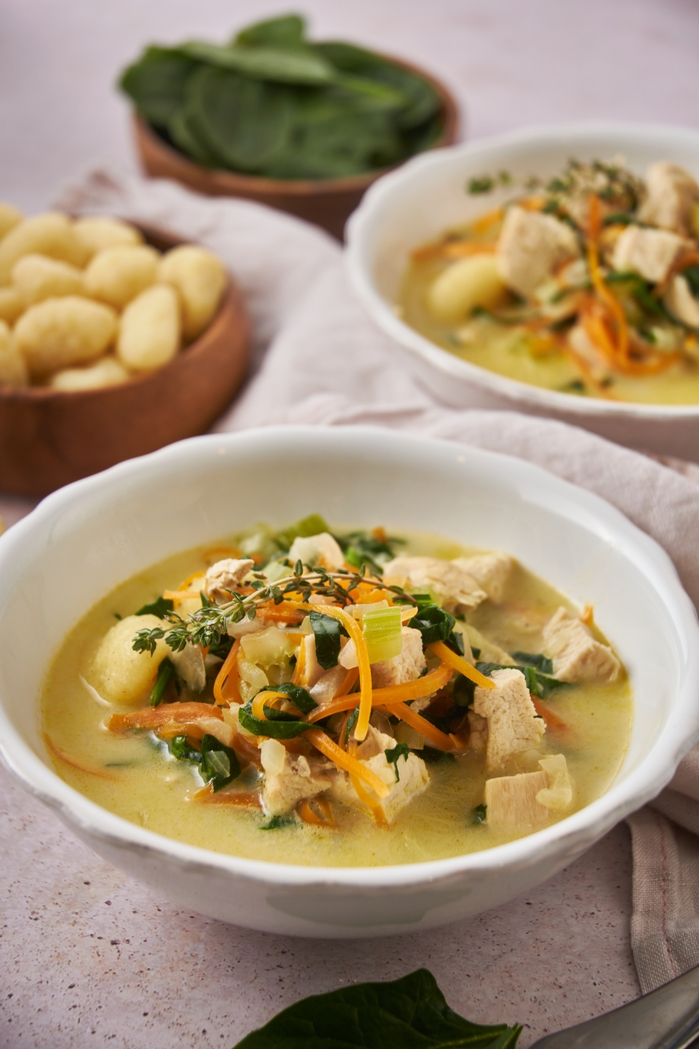 Creamy chicken gnocchi soup in a bowl with carrots, celery, spinach, and fresh herbs on top.