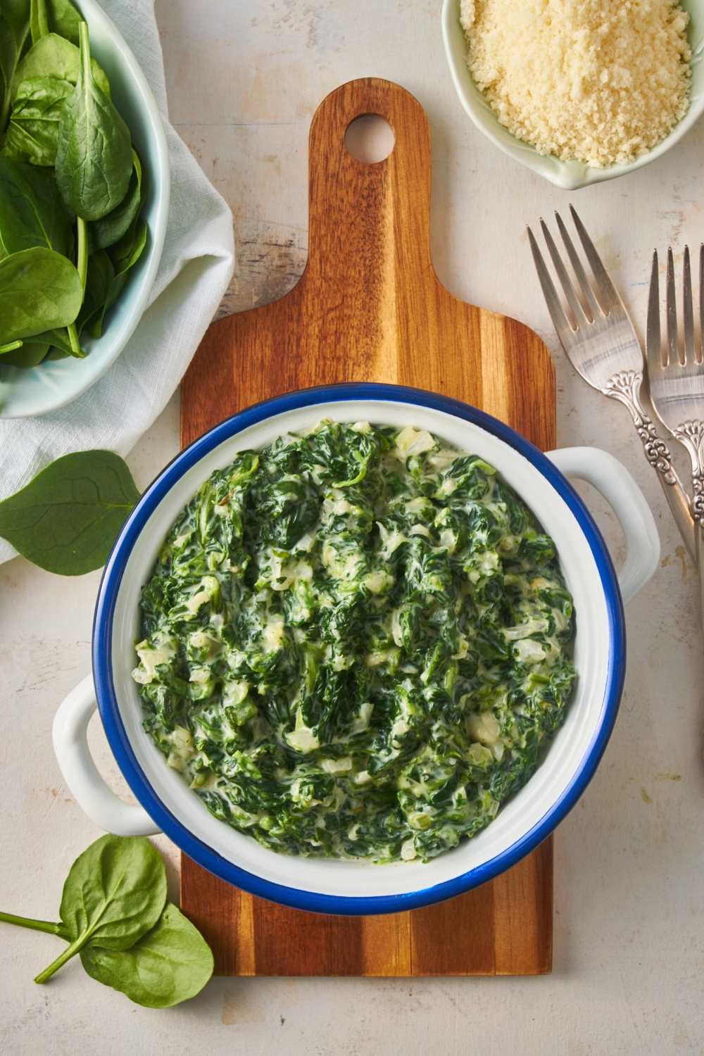 Overhead view of creamed spinach in a white and blue serving bowl atop a wooden board.