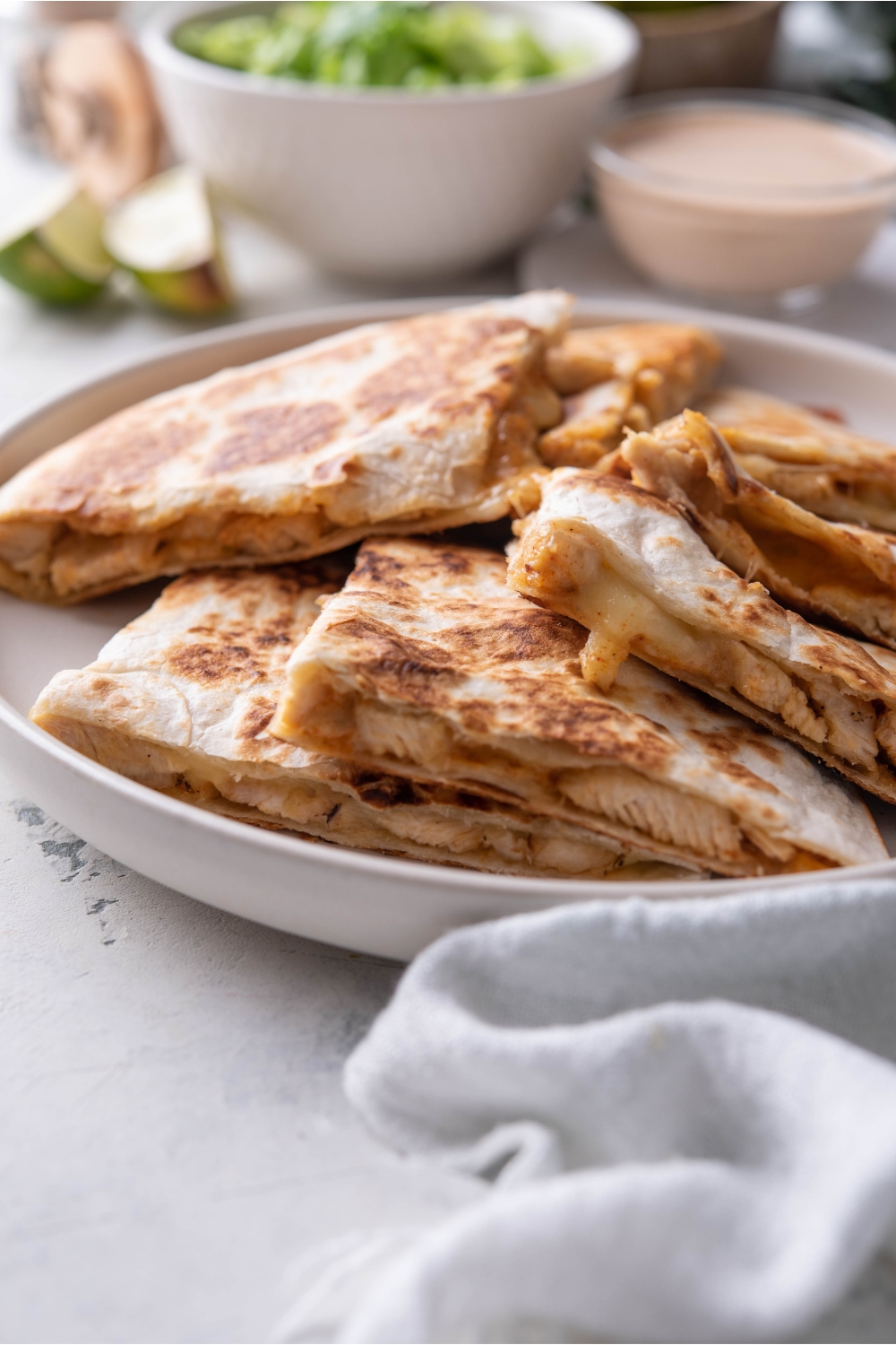 Close up of a plate of chicken quesadilla wedges layered on top of each other on a white plate.