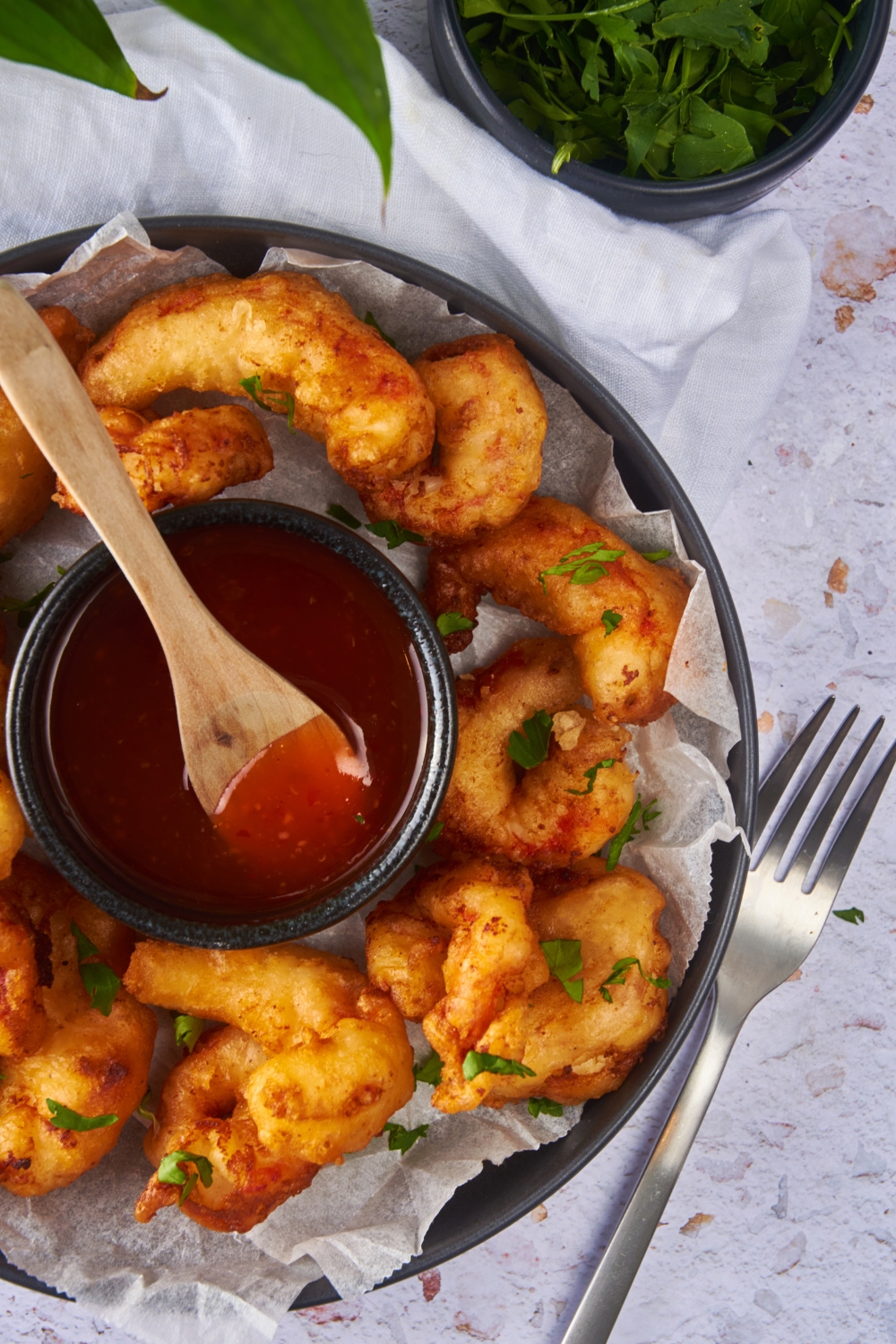 Close up of battered fried shrimp garnished with fresh herbs on a plate with a bowl of sweet and sour sauce.