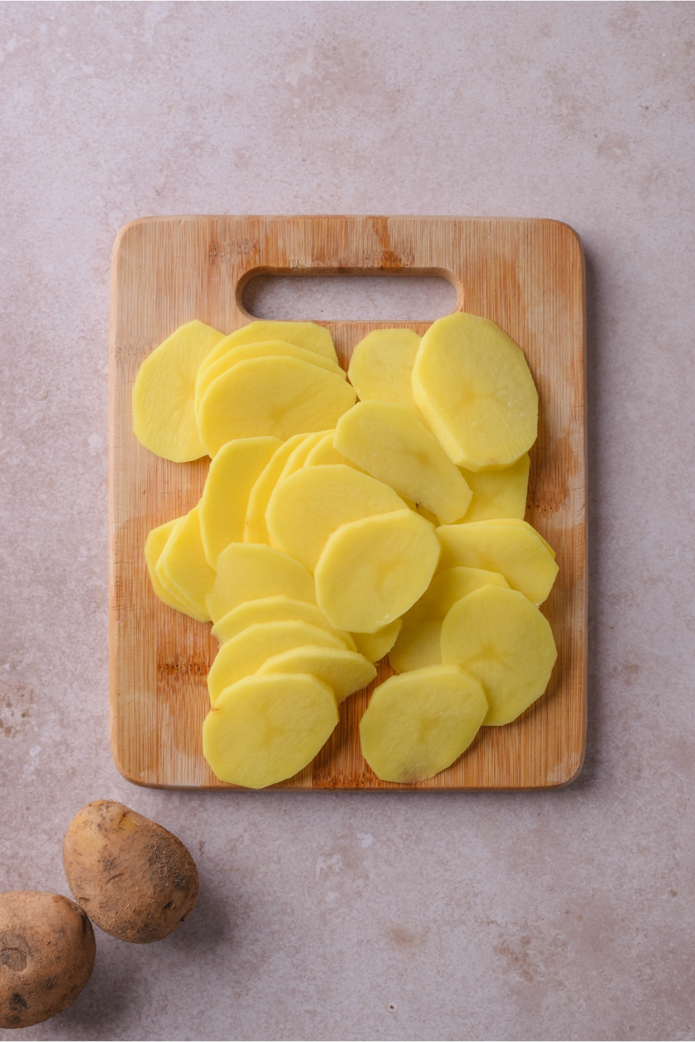 Overhead view of thinly sliced potatoes piled on a wood cutting board.